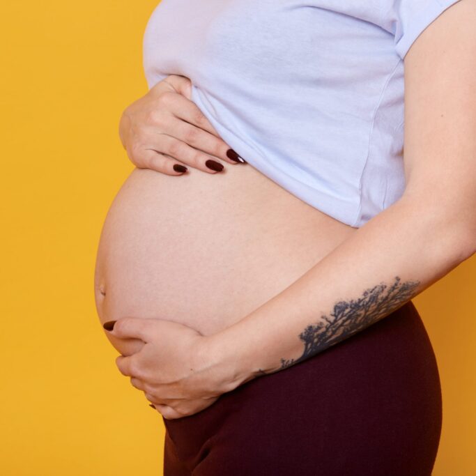 side-view-pregnant-female-with-naked-belly-isolated-yellow-wall-woman-with-tattoo-hend-dressed-casually-being-photographed-motherhood-pragnancy-concept-min pregnancy care